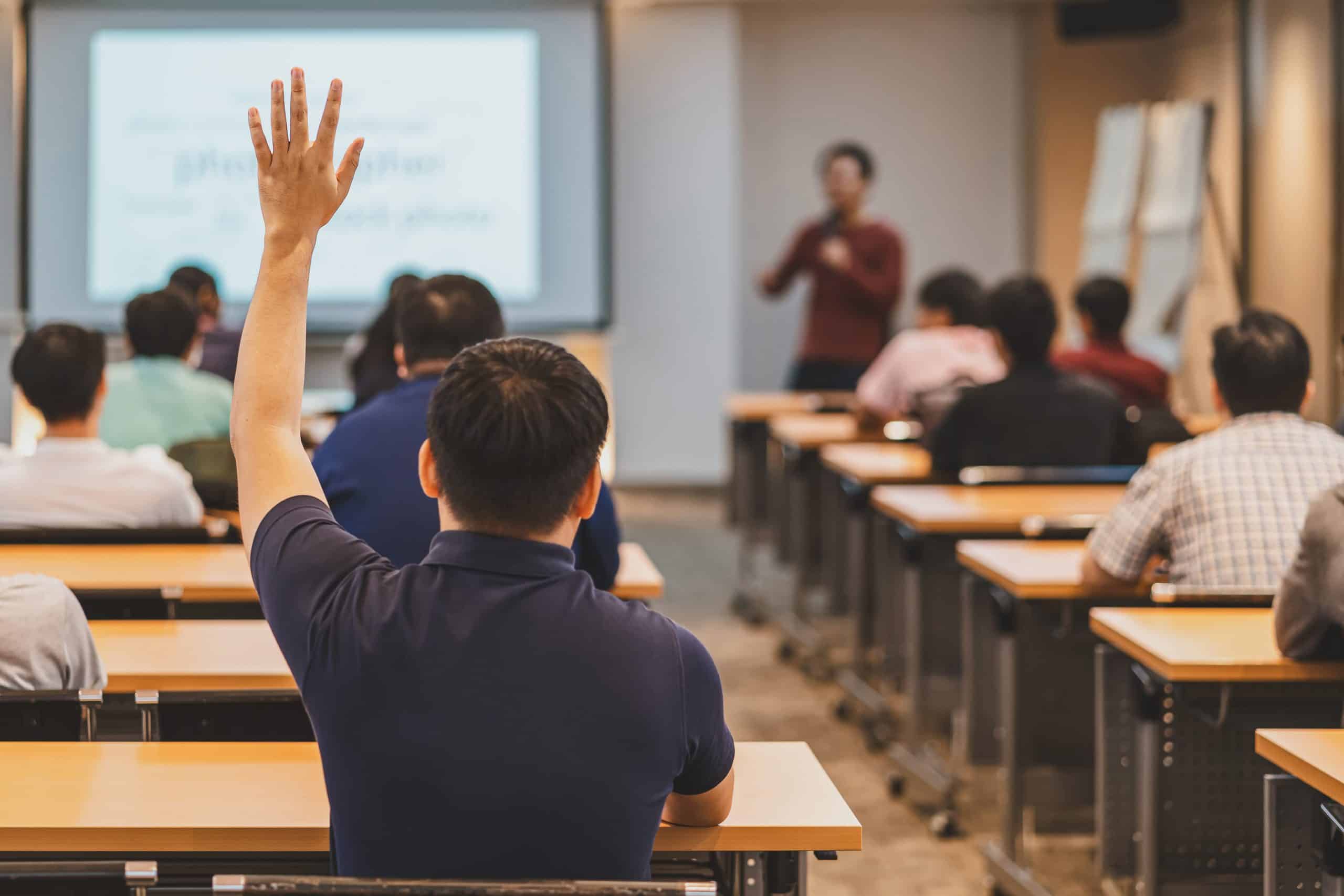 Rear view of Audience in raise hand up response for answer the question in the meeting room or conference hall over speaker on the stage,seminar business and education concept